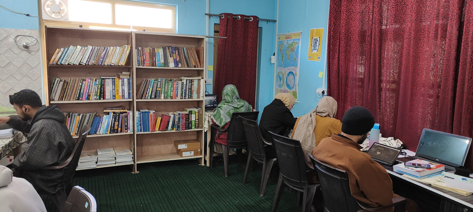 Students working on laptops beside the bookshelves in the resource centre