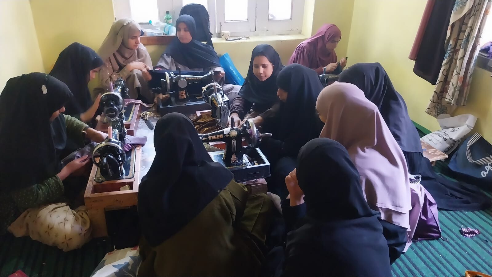 Students gathered around a machine while a trainer demonstrates a stitching technique